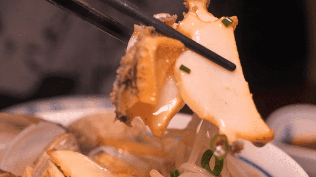 Chopsticks picking up abalone from rice noodle broth