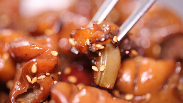 젓가락으로 잡은 윤기 나는 양념 돼지곱창구이