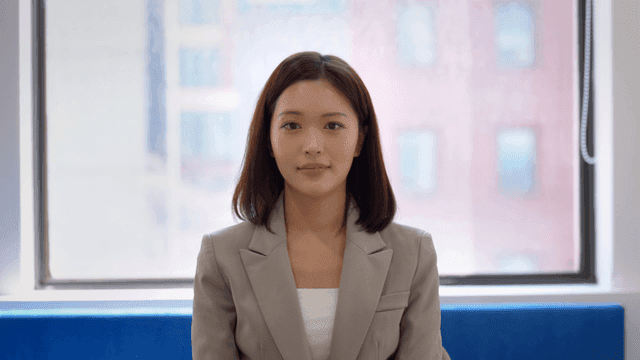 Woman in suit sitting by window and looking straight ahead