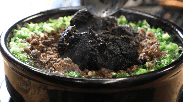 Spoon mixing toppings on stone pot rice
