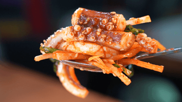 Spoon scooping up spicy seasoned squid with vegetables