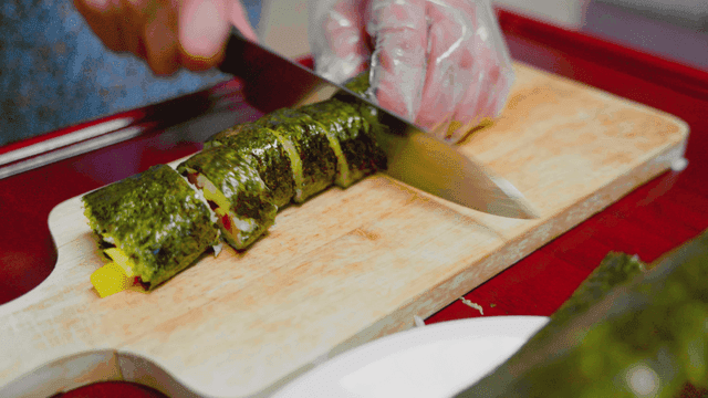 Gimbap being sliced on a wooden board