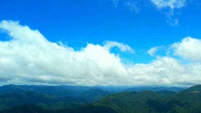 Aerial view of lush green mountains under a bright blue sky with scattered white clouds