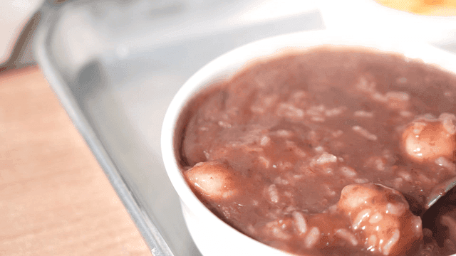 Spoon mixing bowl of red bean porridge with rice cakes