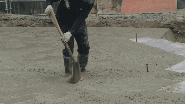 Worker leveling wet concrete with a shovel