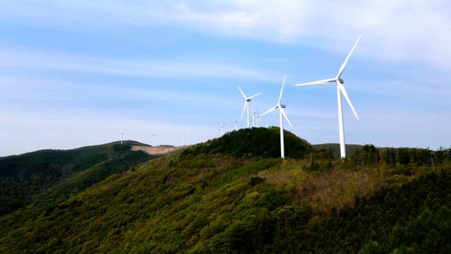 화창한 날 낮의 푸른 산등성이에 설치된 풍력 발전기