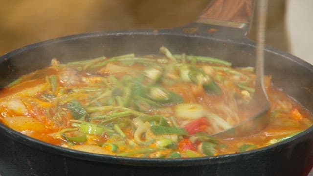 Stirring the spicy fish stew with fresh vegetables using a ladle and spoon