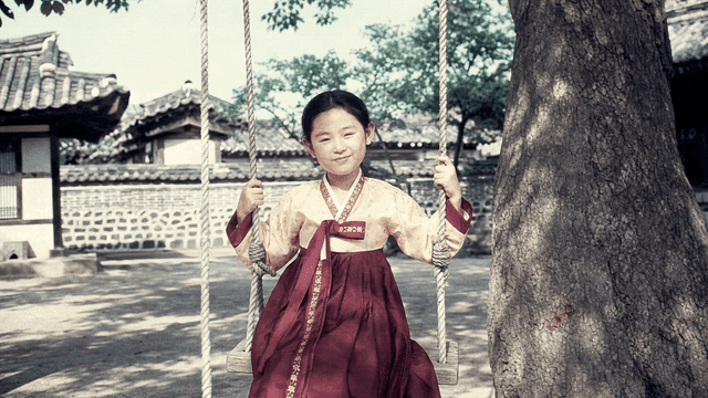 Girl wearing hanbok swinging in traditional courtyard