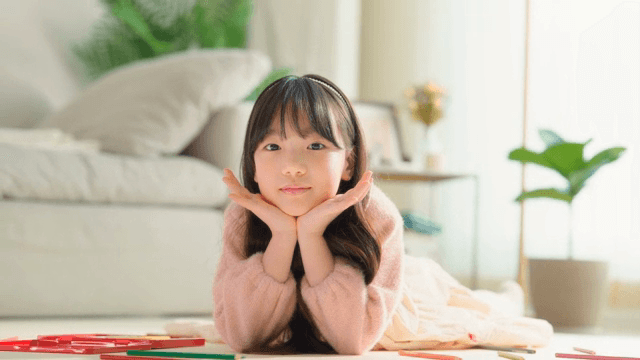 Child lying on the living room floor making a flower pose with their hands