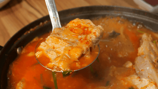 Ladle scooped out spicy fish stew boiling in pot