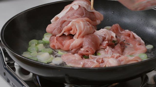 Cooking fresh meat with green onions in a black frying pan