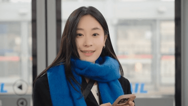 Woman smiling while looking straight ahead at her smartphone on the subway platform