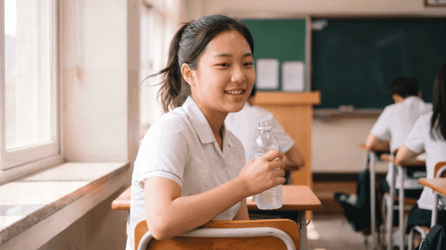 교실에서 땀을 흘리며 물병을 들고 있는 여학생