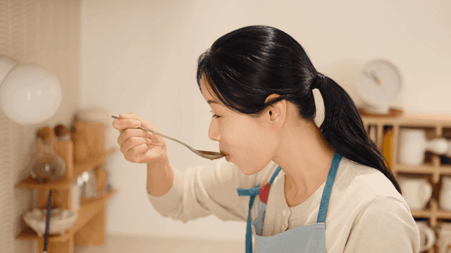 Woman tasting stew in cozy kitchen