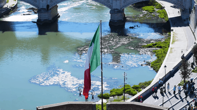Italian flag waving by a riverside bridge