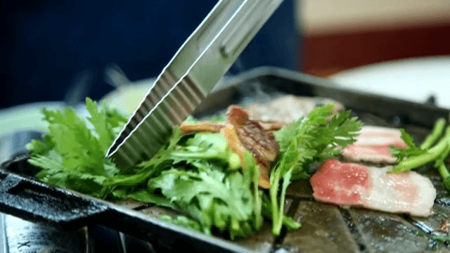 뜨거운 그릴 위에 쑥갓과 함께 삼겹살 굽기