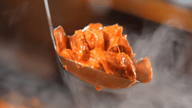 Ladle scooping sausage from budaejjigae broth