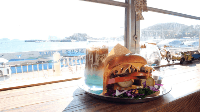 Homemade hamburgers and drinks placed by window overlooking sea