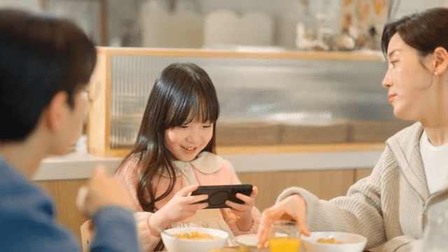 Child who is only focused on her cell phone at the table