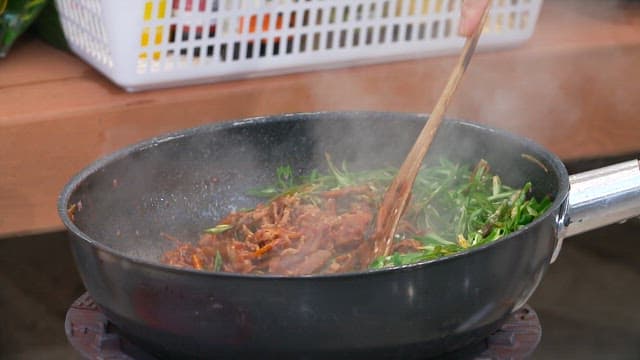 Stir-frying vegetables and meat with spicy seasoning in a wok on the stove