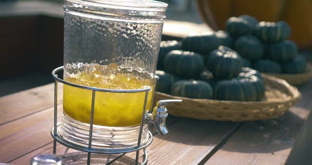 나무 벤치 위의 레모네이드가 담긴 디스펜서와 단호박