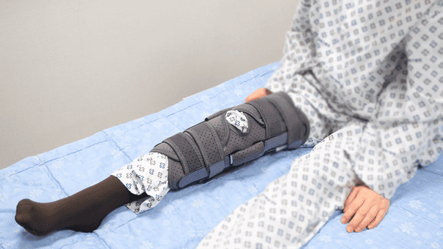 Patient with leg brace on hospital bed