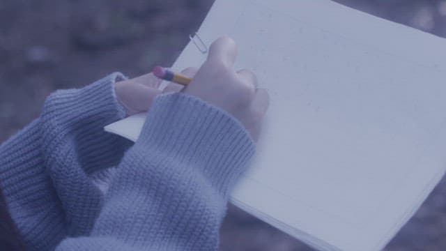 오후에 야외에서 원고지 종이에 연필로 글을 쓰는 사람