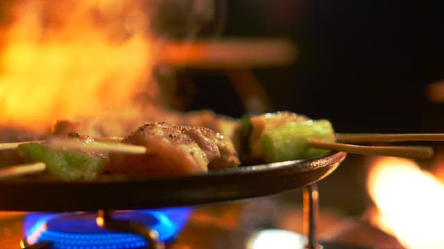 Skewered meat cooking on a pan over a gas burner at night