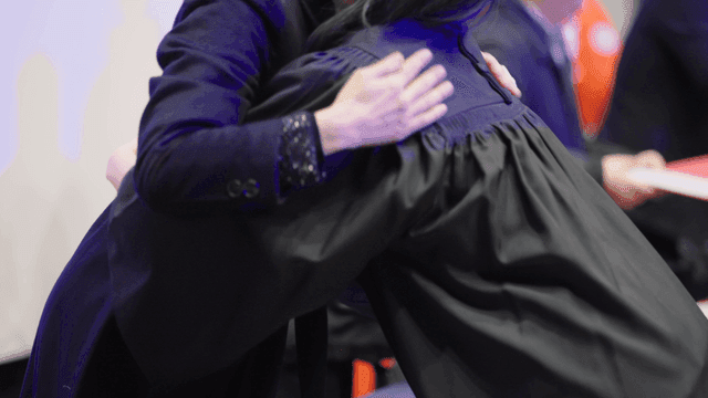 Professors and graduates warmly embrace at graduation ceremony.