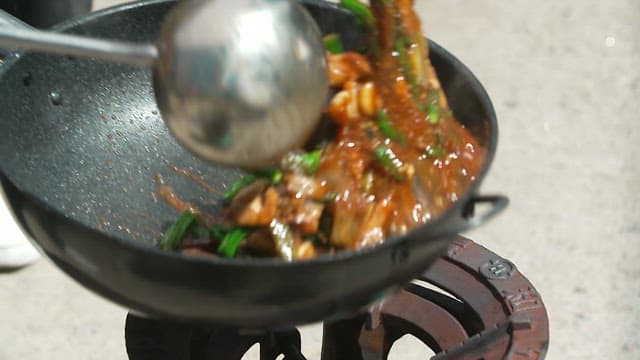 Braised spicy chicken with chili peppers cooked in a large wok and ladle