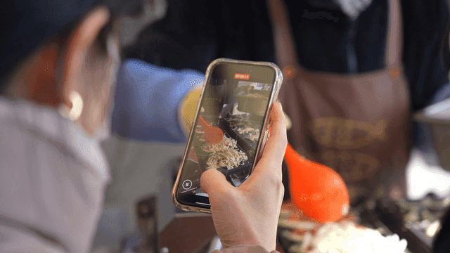 Person taking picture of himself cooking bungeoppang street food with his cell phone.