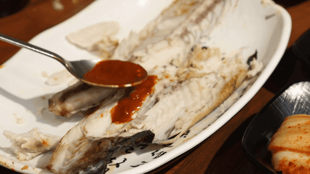 Grilled Spanish mackerel coated with spicy sauce using spoon