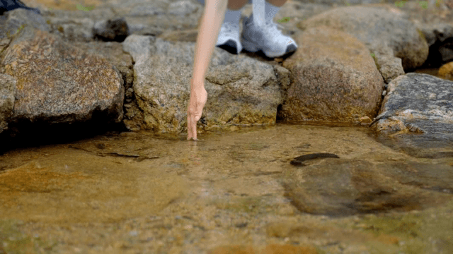 A person touching water in a rocky stream