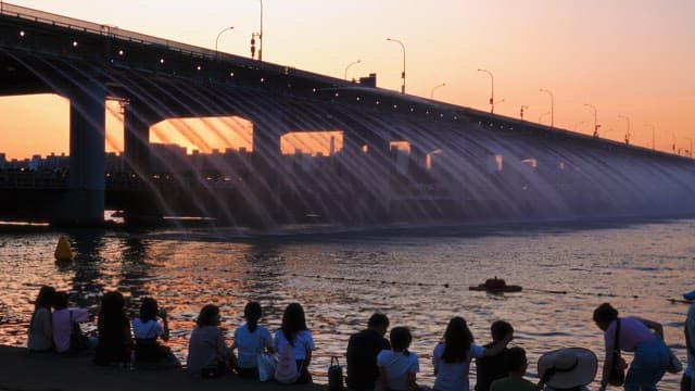 People watching water fountain show on a bridge at sunset