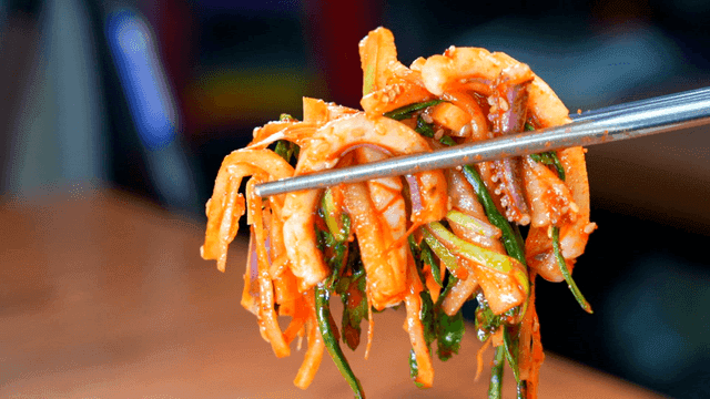 Chopsticks picking up spicy seasoned squid on plate