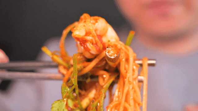 Person scooping up spicy bibimyeon with chopsticks