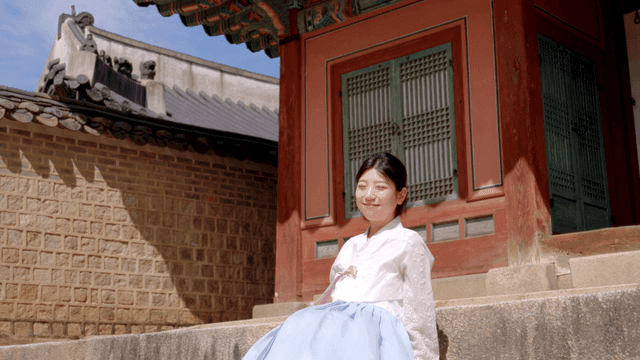 한국 전통 건물 옆에 앉아 있는 한복 입은 여성