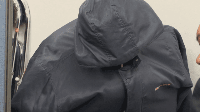 Person wearing hooded jacket indoors and covering his face