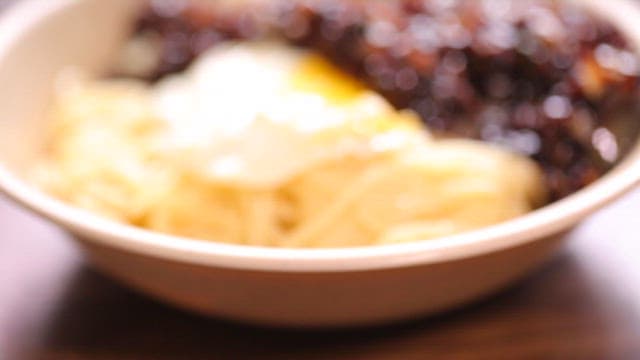 Bowl of noodles in thick black bean sauce with a fried egg