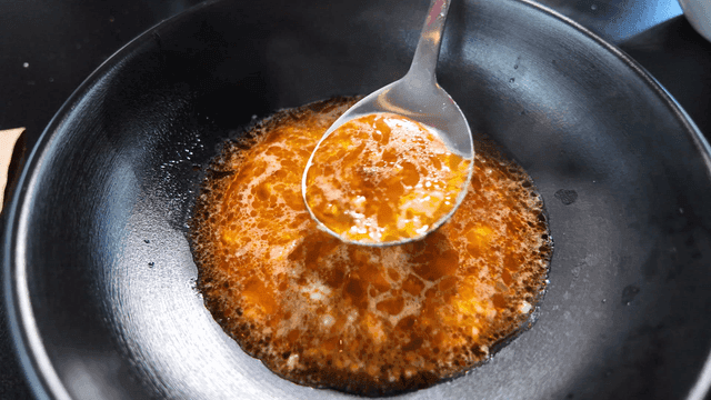 Spoon scooping hot mala stew broth from black bowl