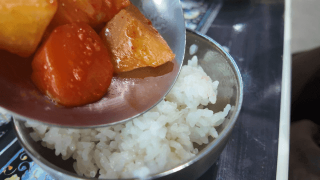 Ladle with spicy chicken stew potatoes and carrots on top of rice