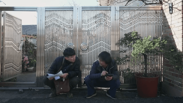 문 옆에 쪼그려 앉아 대화하는 두 남자