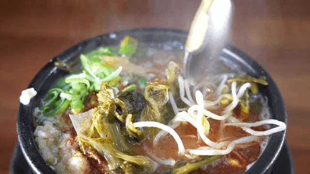 Spoon mixing beef hangover soup in earthenware pot