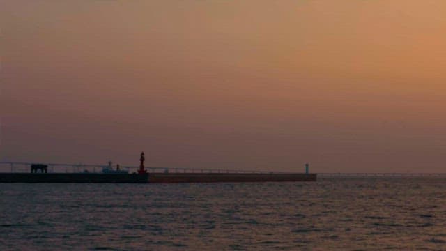 멀리 등대와 부두가 보이는 고요한 해변의 일몰