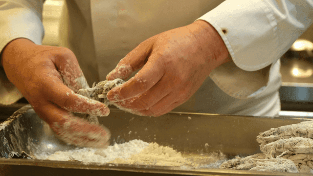 Chef coats crab and shrimp in flour.