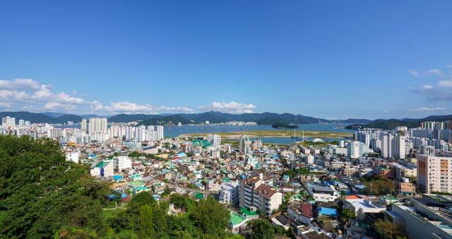 낮부터 밤까지의 하늘 아래 건물과 산, 바다가 있는 도시 경관