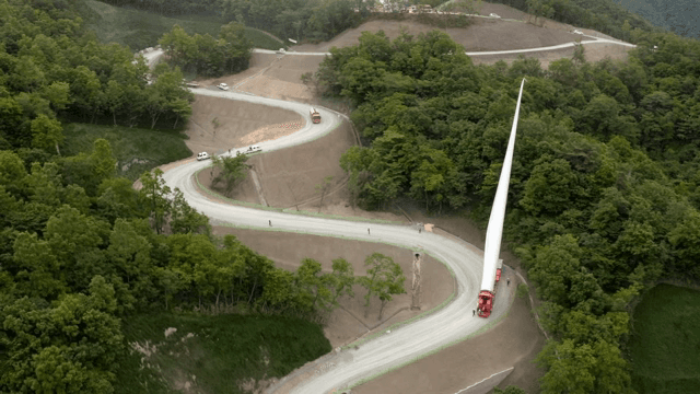 울창한 숲 속 구불구불한 도로에서 풍력 터빈 자재를 운반하는 모습