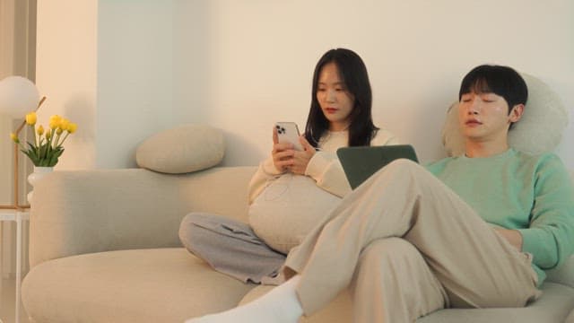 Two people using digital devices on a sofa in cozy living room