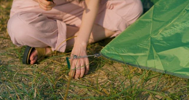 Woman Hammering a Tent Peg into the Ground with Grass