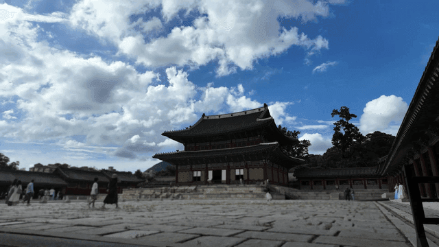 Tourists viewing traditional Korean palace under blue sky.